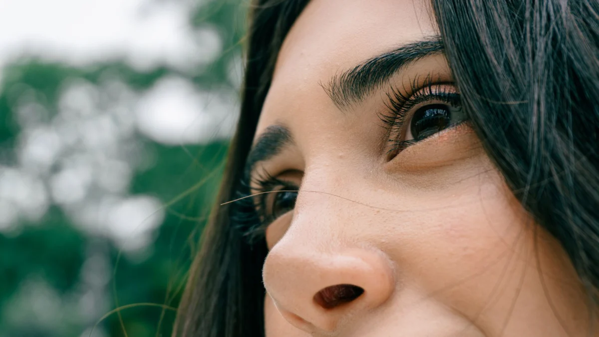 Een close-up van het gezicht van een vrouw tegen een weelderige groene achtergrond, wat een gevoel van rust oproept.