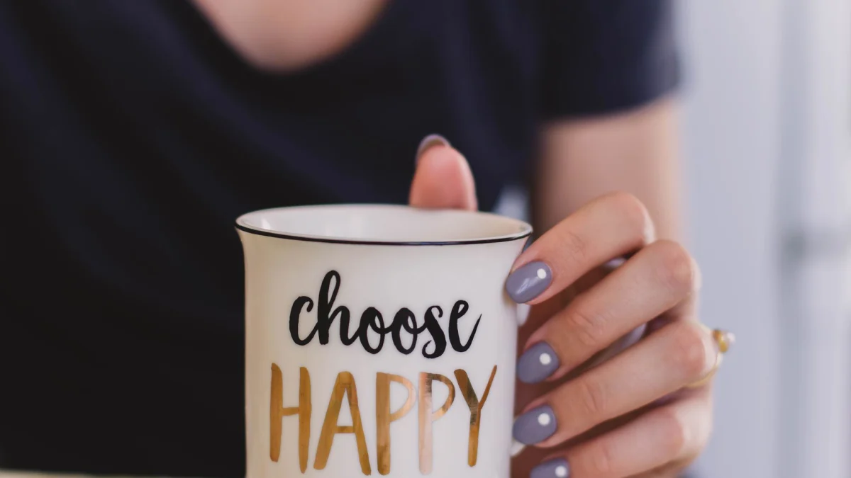 Een vrouw houdt een mok met de tekst 'kies gelukkig' binnenshuis vast, wat positiviteit bevordert.