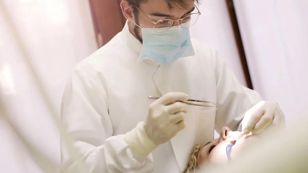 Een tandarts in een masker en handschoenen die een patiënt behandelt in een tandartspraktijk binnenshuis.