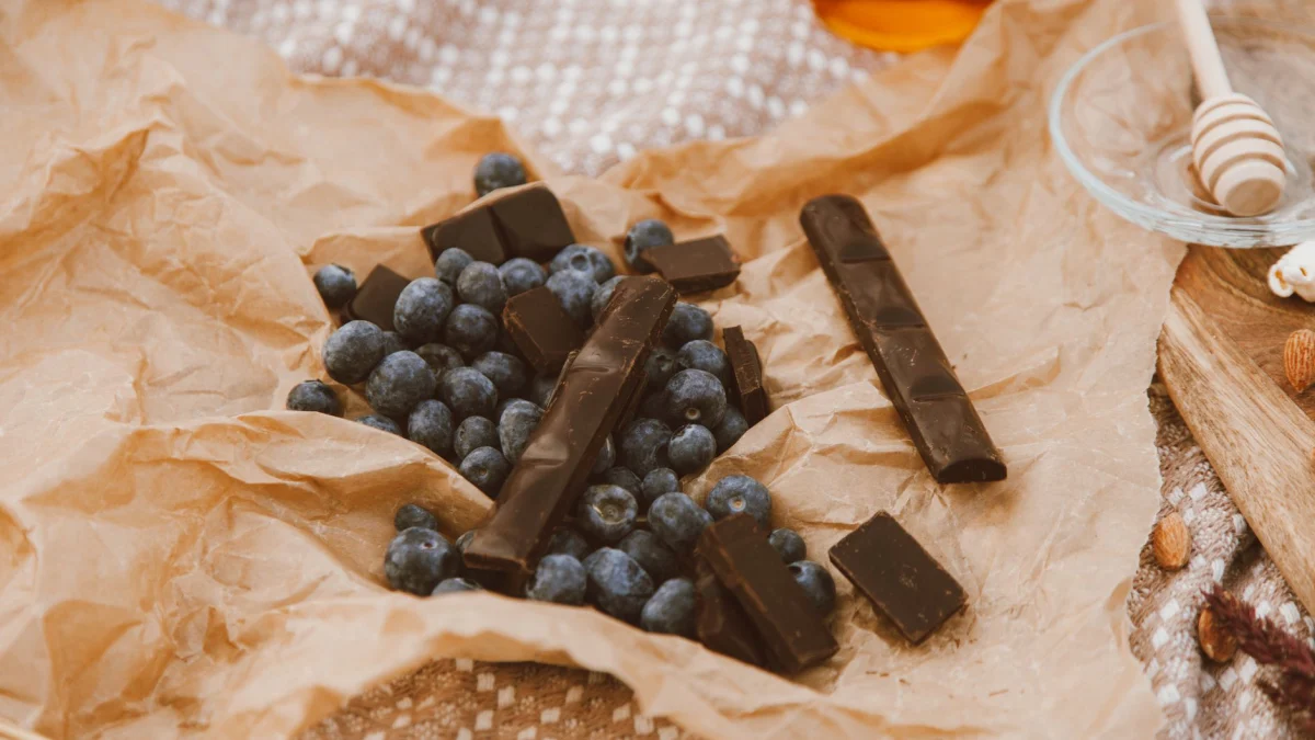Een artistiek stilleven van blauwe bessen en donkere chocolade op perkamentpapier, perfect voor foodliefhebbers.