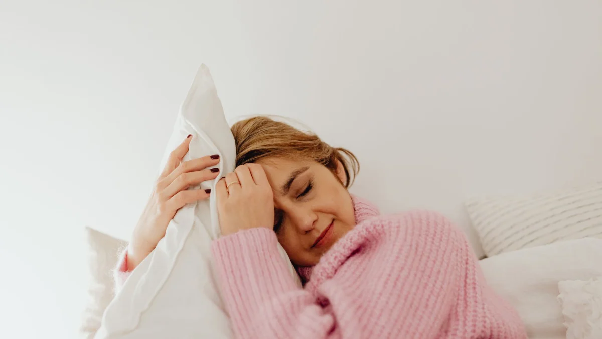 Vrouw die vredig rust met een gezellige roze trui en kussen, straalt kalmte en ontspanning uit.