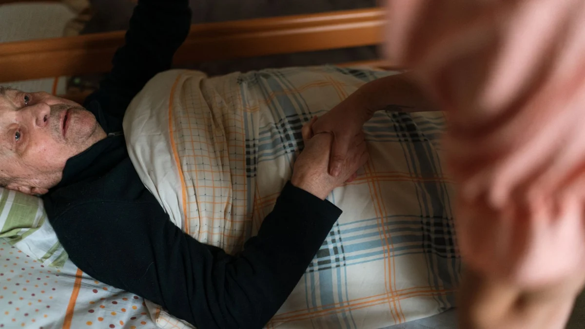 Een mantelzorger houdt de hand vast van een oudere volwassene en biedt thuis steun en geruststelling.