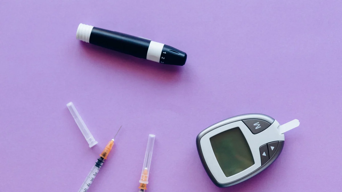 Bovenaanzicht van diabetesbeheer tools, waaronder glucosemeter en insuline spuiten op paarse achtergrond.