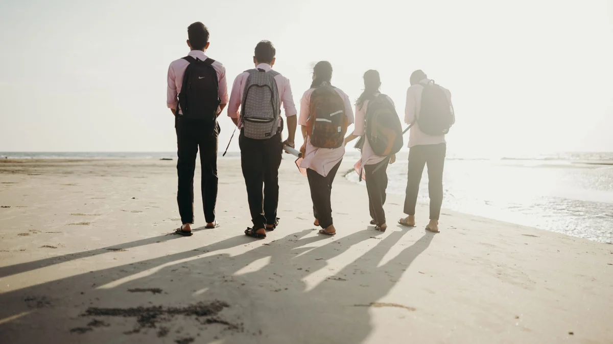 Een groep vrienden met rugzakken geniet van een zonnige dag terwijl ze langs de strandlijn wandelen.