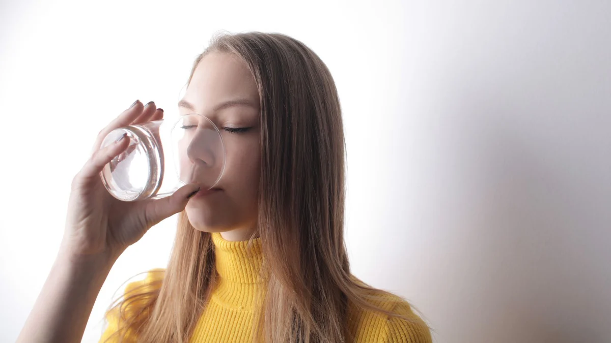 Een vrouw in een gele trui drinkt moeiteloos water binnen, wat zuiverheid en verfrissing toont.