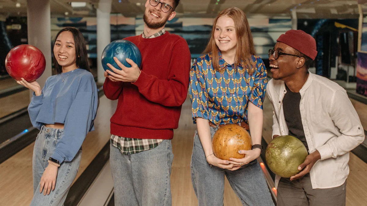 Vier vrienden hebben plezier in een bowlingbaan, houden kleurrijke bowlingballen vast en lachen.