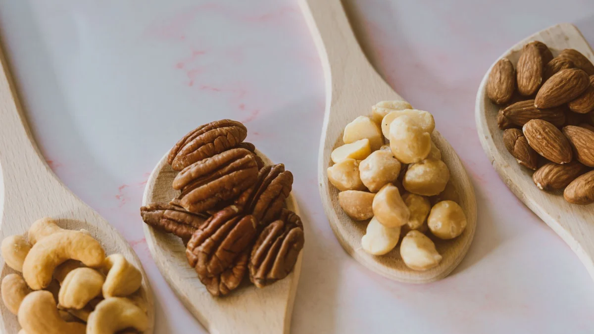 Close-up van diverse noten zoals amandelen, pecannoten, cashewnoten en macadamianoten op houten lepels.