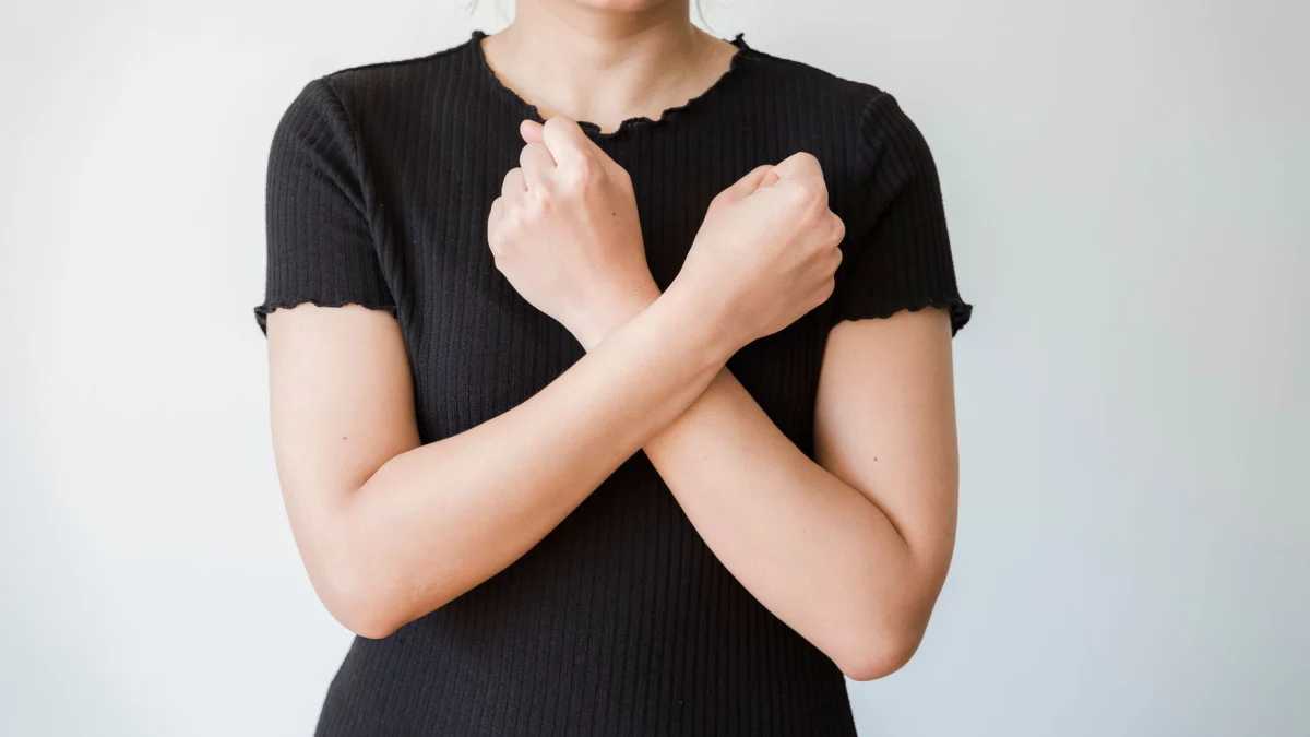 Een vrouw in een zwart shirt met crossed arms voor een eenvoudige witte achtergrond.
