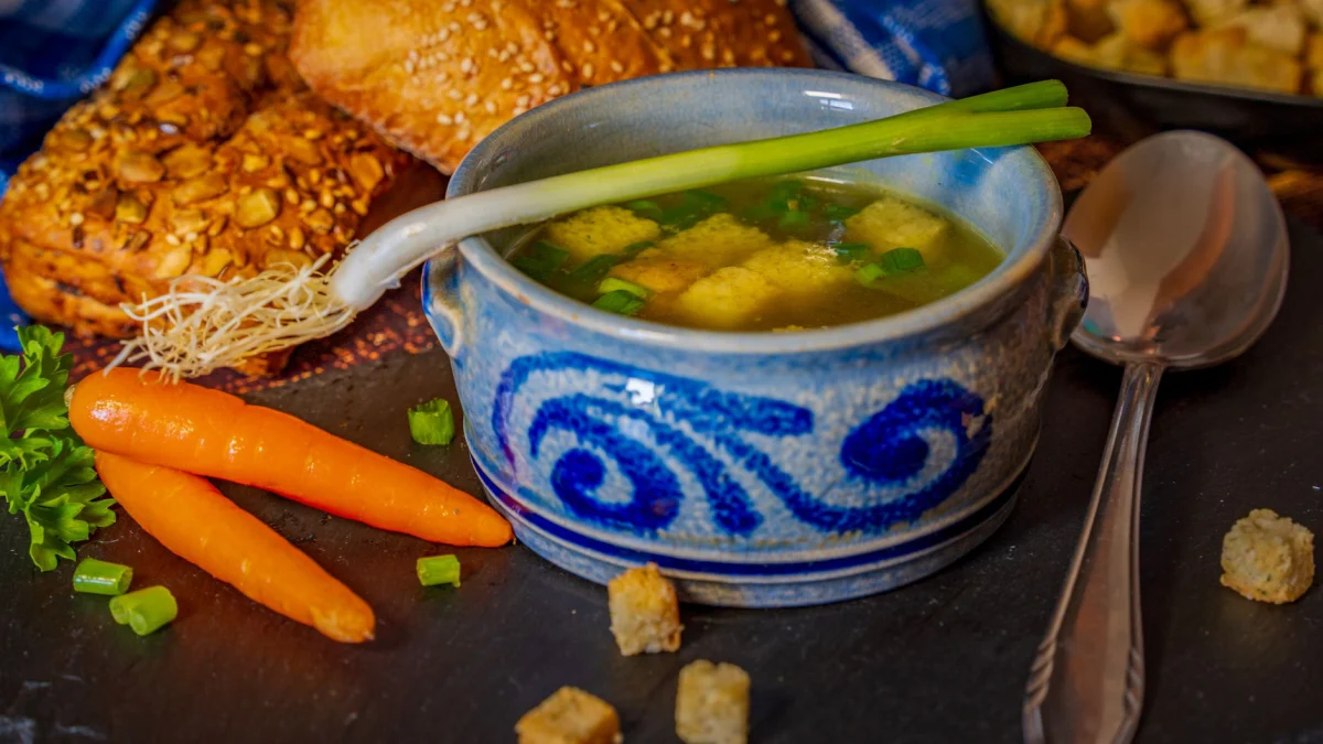 Gezellige kom groentebouillon met croutons en brood, perfect voor wintercomfort.