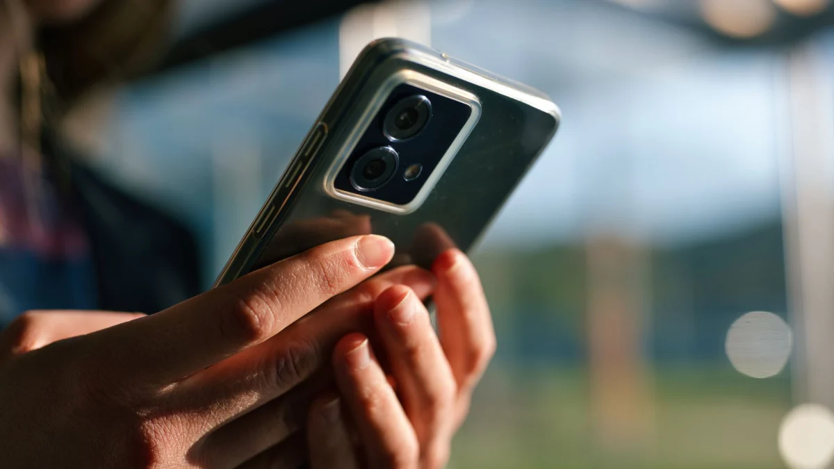 Scherpe opname van handen die een moderne smartphone vasthouden, buiten, met een wazige achtergrond.