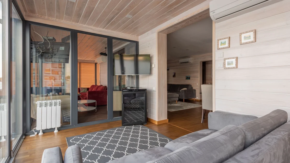 Ruime moderne woonkamer met glazen deuren, houten plafonds en elegante inrichting.