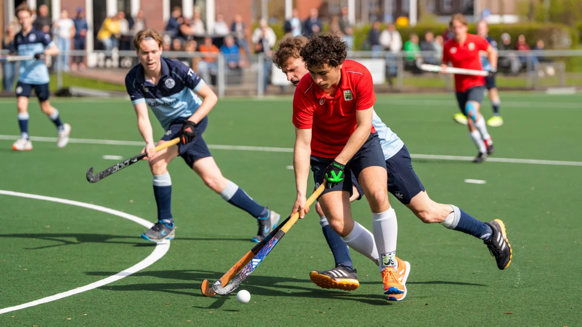 Onder de stralende zon strijden de atleten in een dynamische hockeywedstrijd, waarbij teamwork en vaardigheid centraal staan.