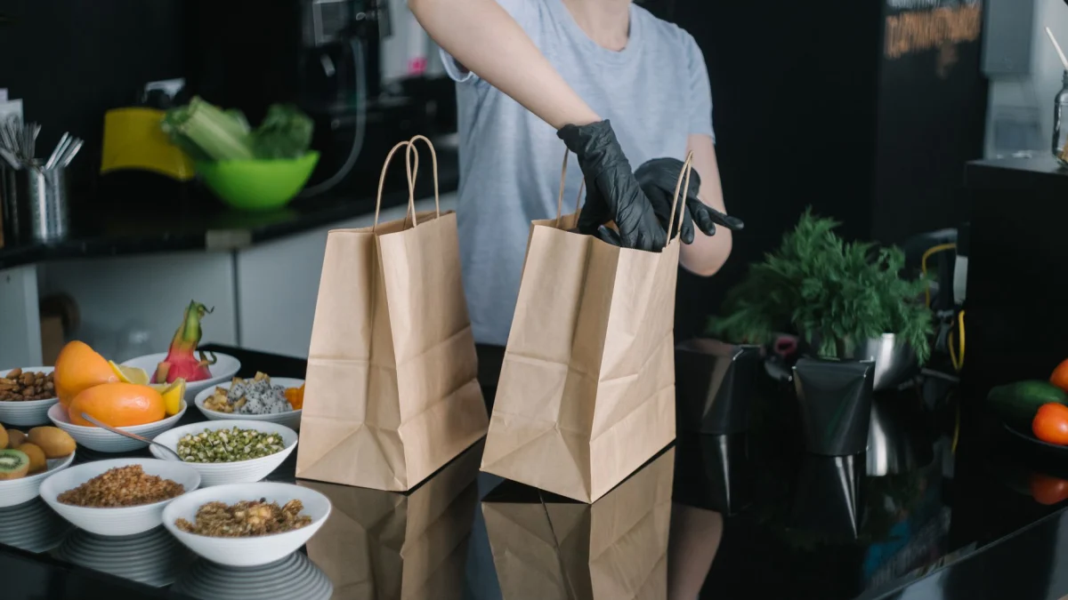 Een persoon in een keuken pakt ingrediënten in papieren tassen voor afhaalbestellingen.