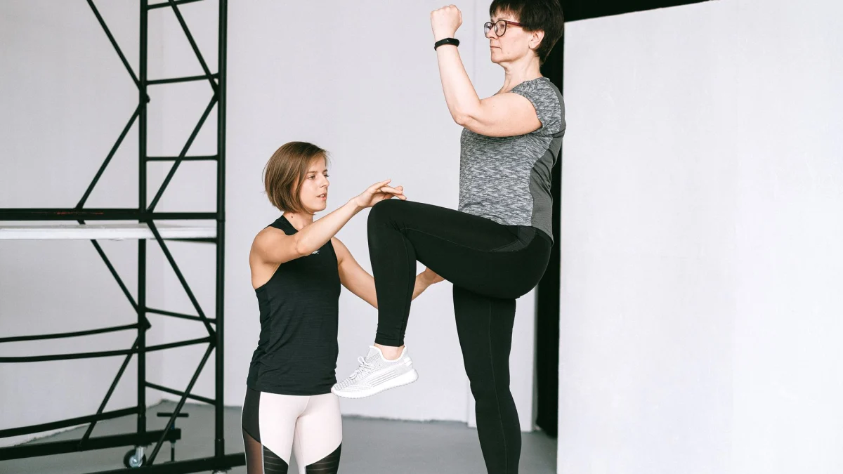 Een oudere vrouw voert oefeningen uit met een fitnesscoach, met focus op een gezonde levensstijl en welzijn binnenshuis.