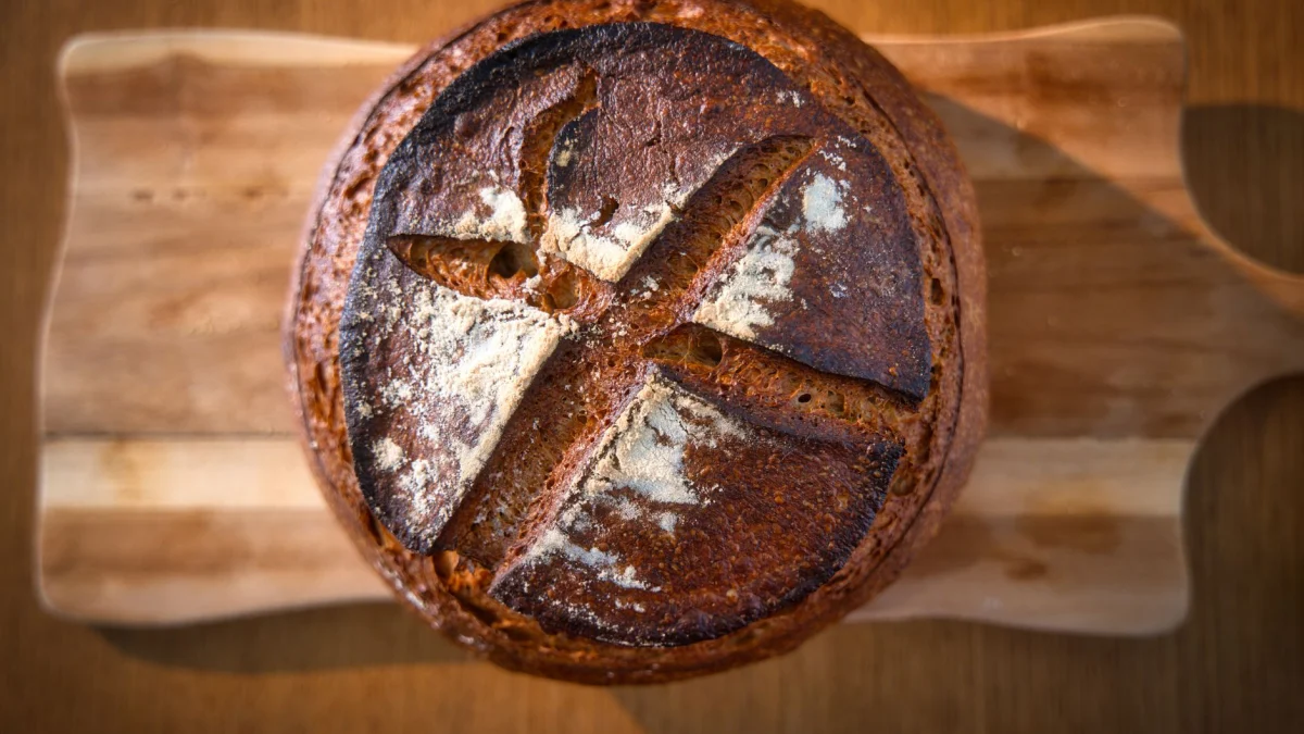 Close-up van een versgebakken ambachtelijk brood op een houten plank, waarbij de knapperige textuur en het rustieke karakter goed tot hun recht komen.