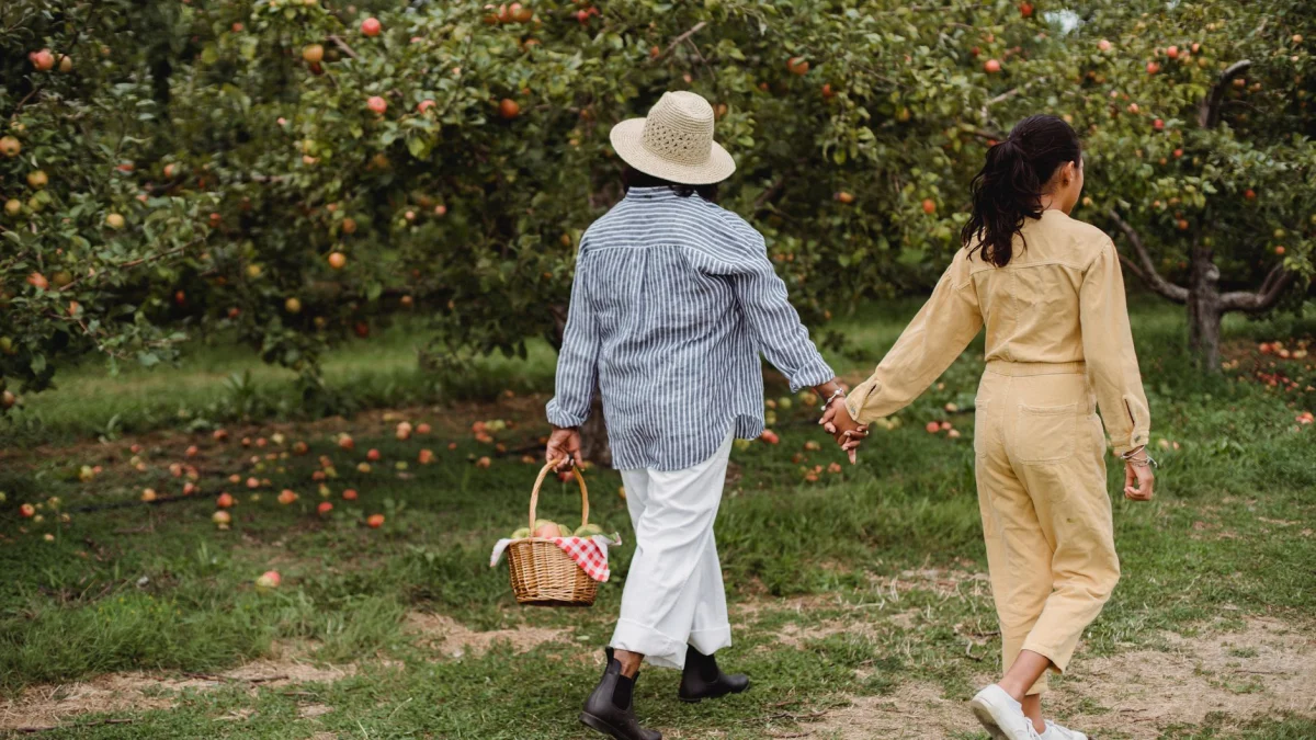 Een moeder en dochter hand in hand wandelend door een weelderige appelboomgaard met een mand.