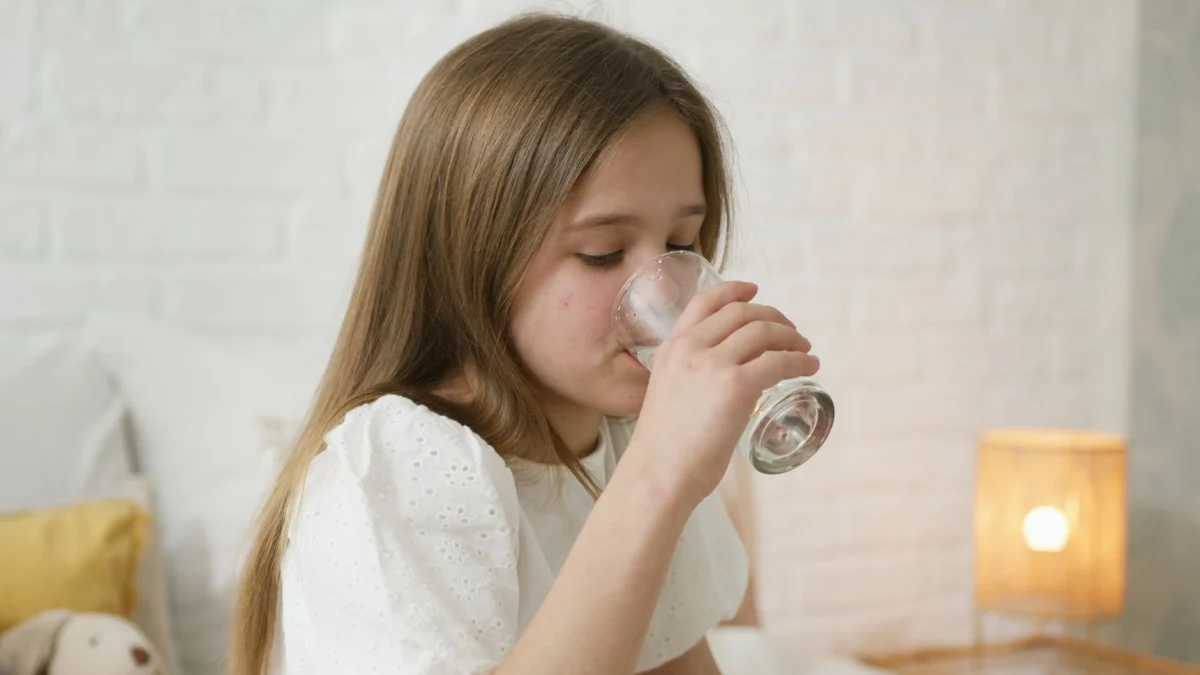 Een jong meisje drinkt water in een gezellige slaapkamer, met nadruk op hydratatie en comfort.