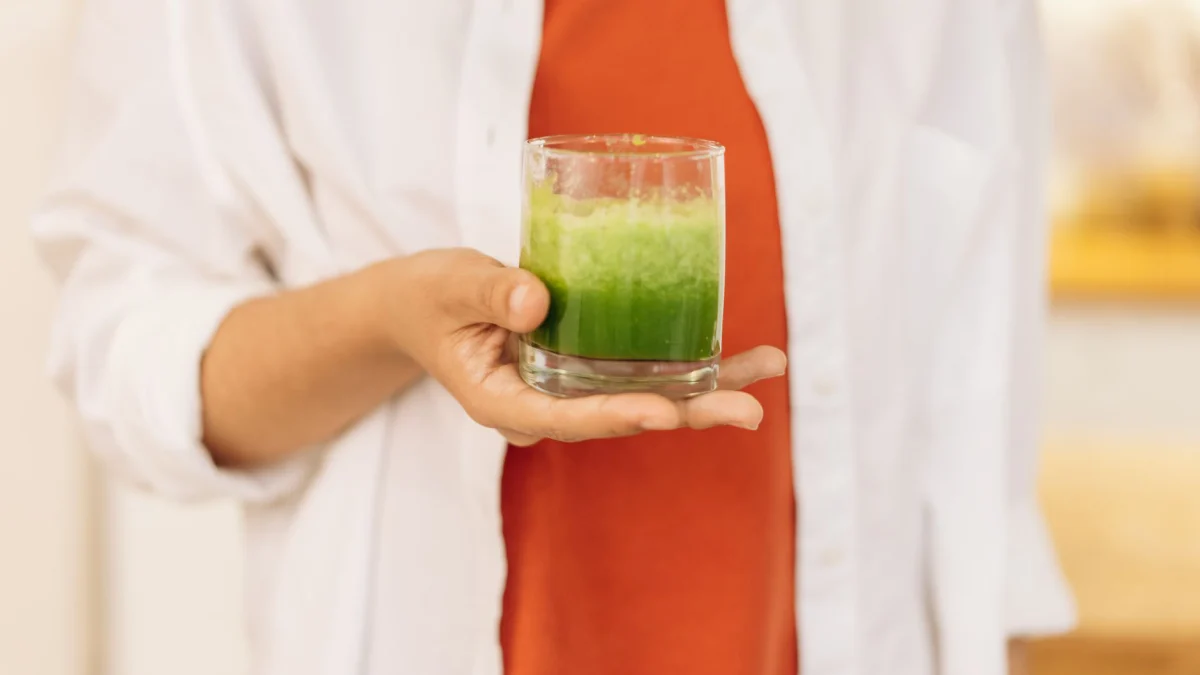 Close-up van een persoon die een verfrissende groene smoothie vasthoudt, symbool voor een gezonde levensstijl.