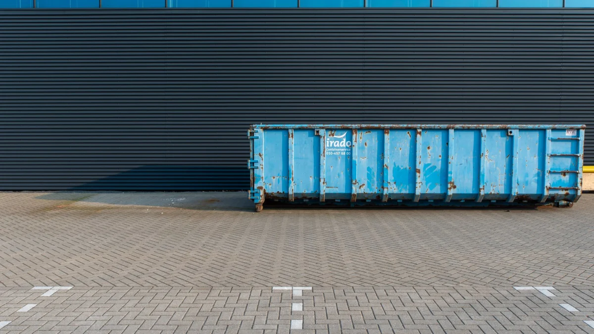 Een blauwe industriële container geplaatst naast de gevel van een modern gebouw, met schone lijnen en een stedelijke omgeving.