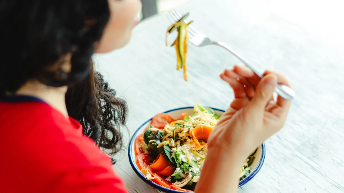 Een vrouw in een rode shirt geniet binnen aan de tafel van een restaurant van een verse salade.