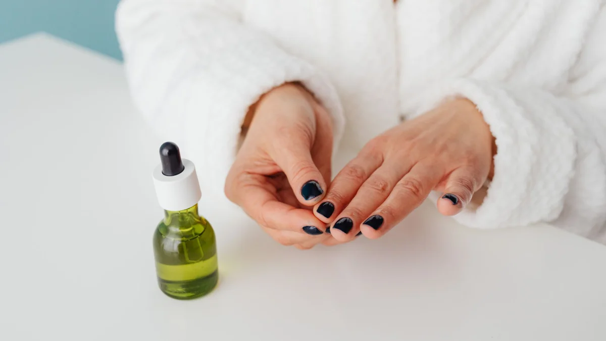 Vrouw in badjas die serum aanbrengt met een groene glazen fles, met een focus op haar zelfverzorgingsroutine.