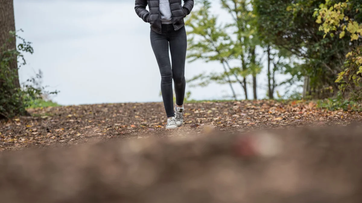 Een vrouw loopt langs een schilderachtig bospad tijdens de herfst en vangt de essentie van buitenleven en fitness.