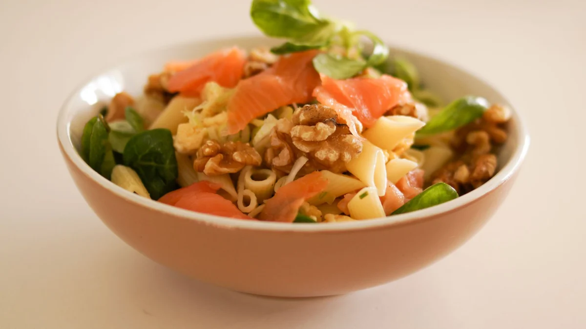 Heerlijke pastasalade met gerookte zalm, walnoten en verse groenten in een keramische kom.