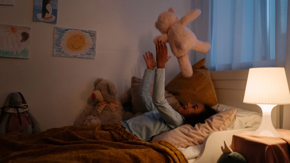 Een jong meisje speelt gelukkig met een teddybeer in haar gezellige slaapkamer 's nachts.