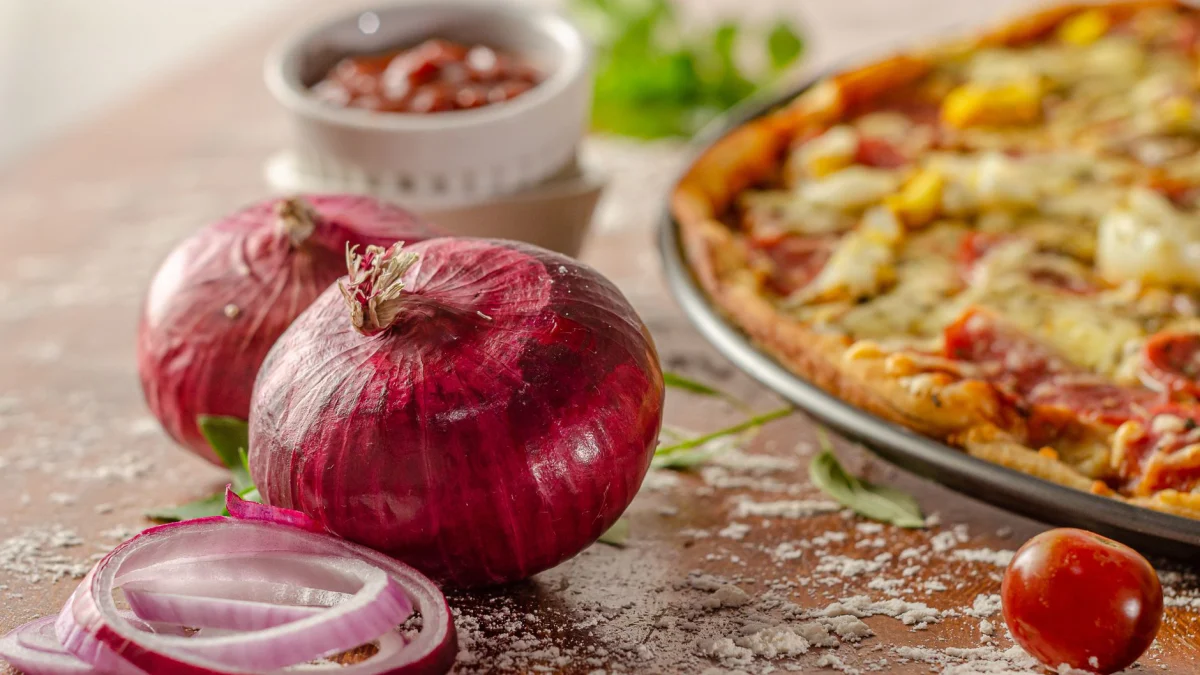 Rode uien en verse tomaten gerangschikt naast een heerlijke pizza, ideaal voor voedsel fotografie.