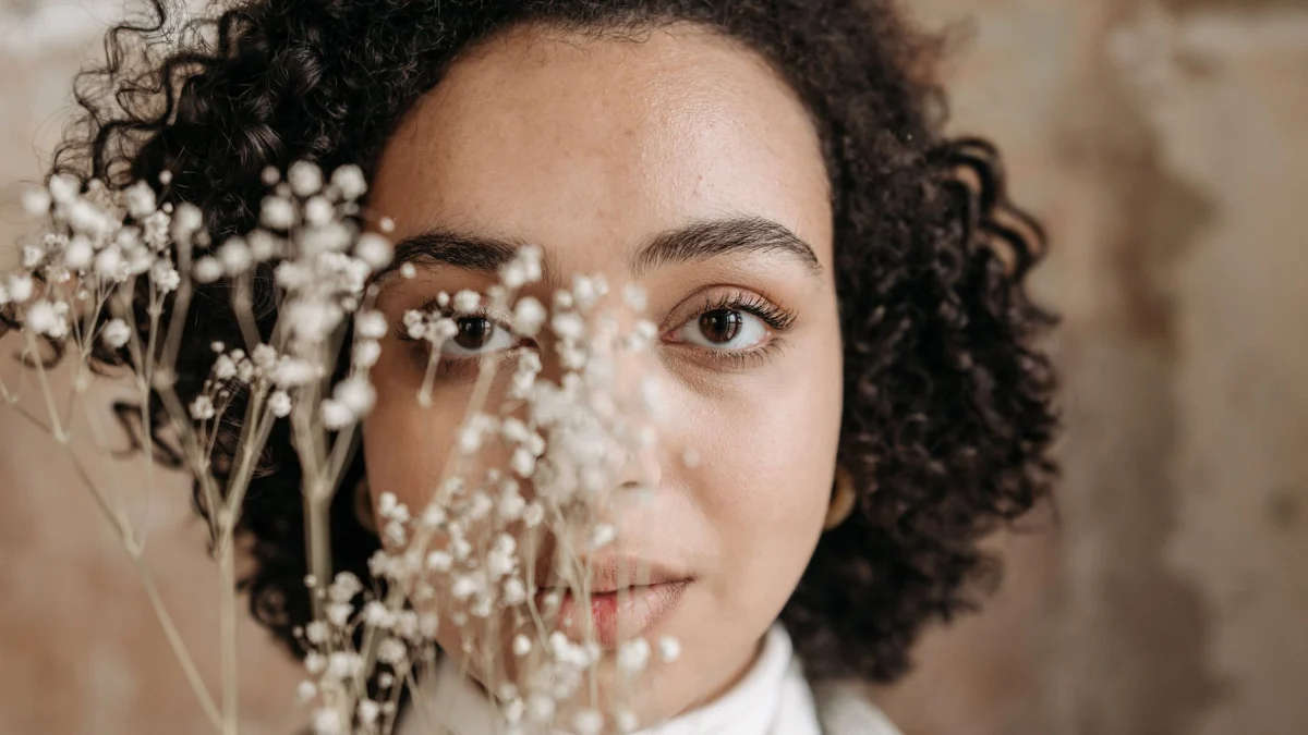 Close-up portret van een vrouw met krullend haar, gedeeltelijk verborgen achter delicate bloemen.
