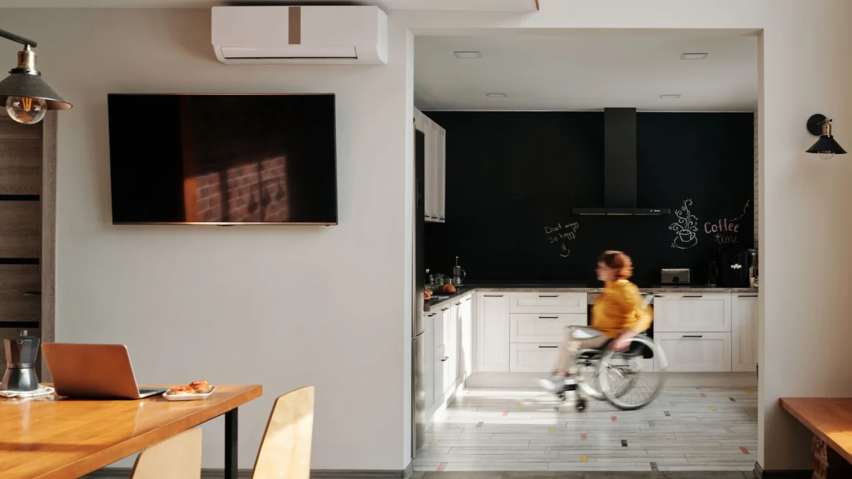 Een vrouw in een rolstoel beweegt door een moderne, stijlvolle keuken met witte kasten.