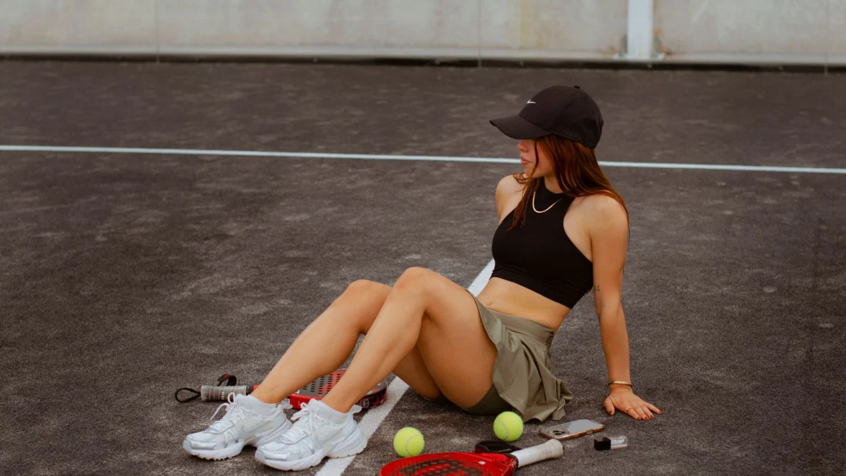 Jonge vrouw zit op een tennisbaan met rackets en tennisballen en geniet van een ontspannen moment in de buitenlucht.
