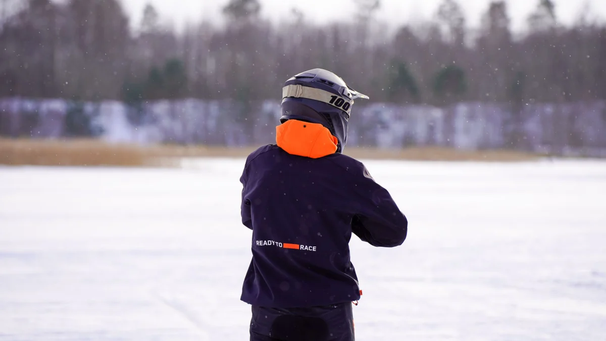 Een rijder in beschermende kleding staat op een besneeuwd veld in Letland, klaar voor een ijsrace.