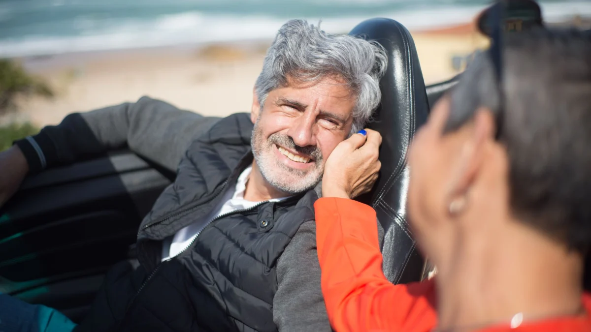 Oudere stel lachend en genietend van een rit in een cabriolet aan het strand in Portugal.