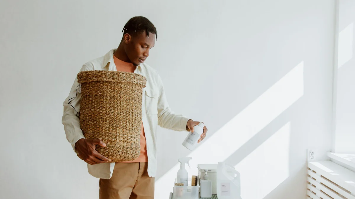 Een man houdt een wasmand vast terwijl hij binnen schoonmaakproducten selecteert