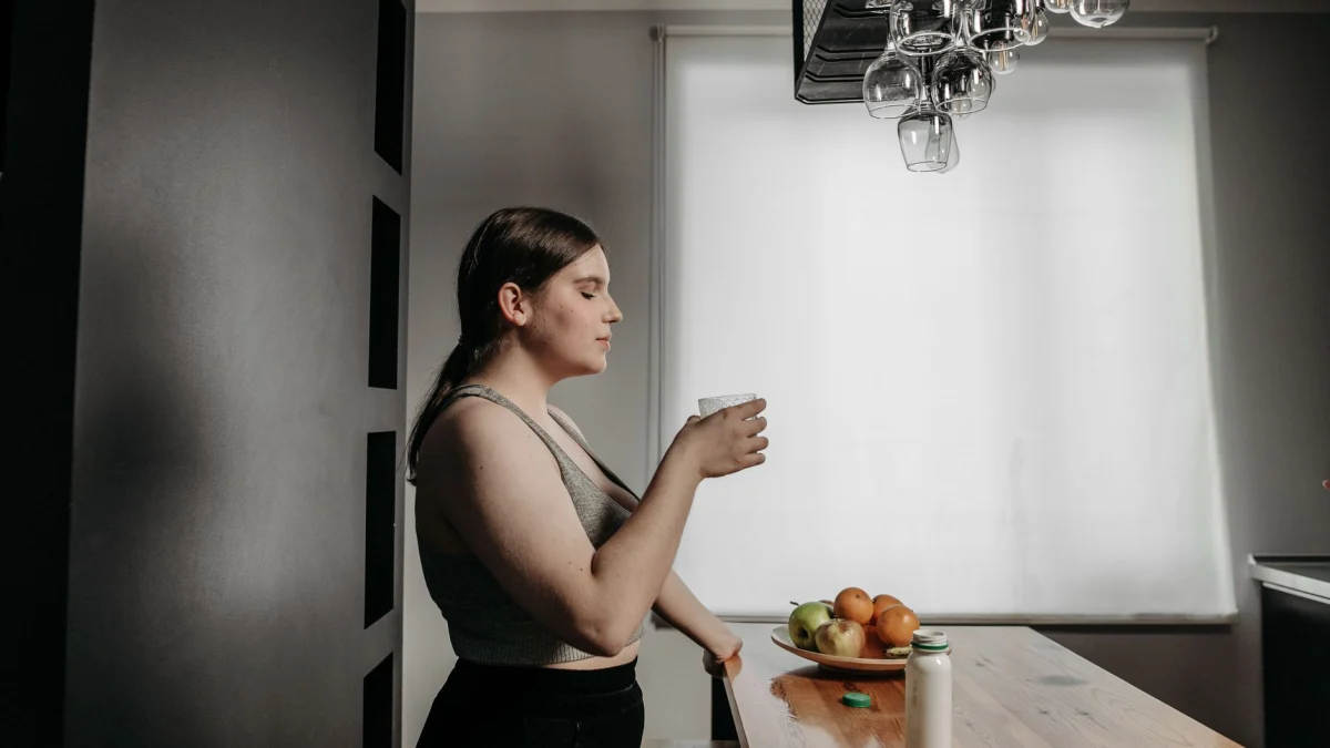 Een vrouw met gesloten ogen geniet van een smoothie en omarmt een gezonde levensstijl in de keuken.
