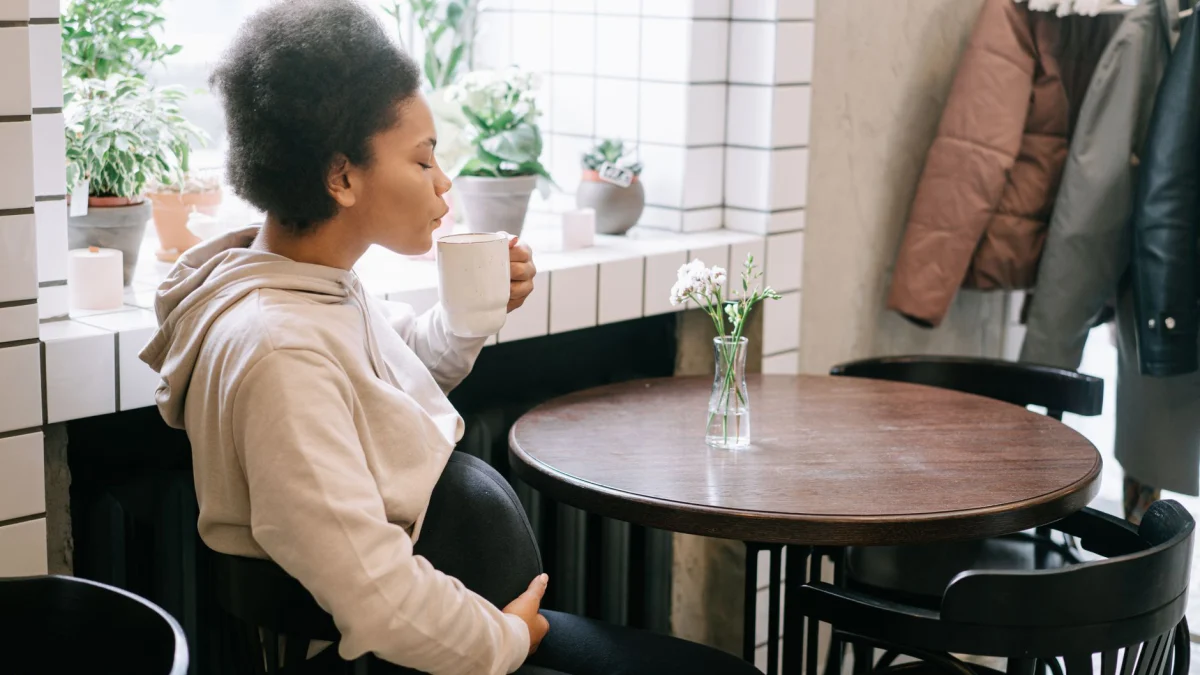 Zwangere vrouw ontspant met koffie in een gezellige cafésetting, omringd door planten.
