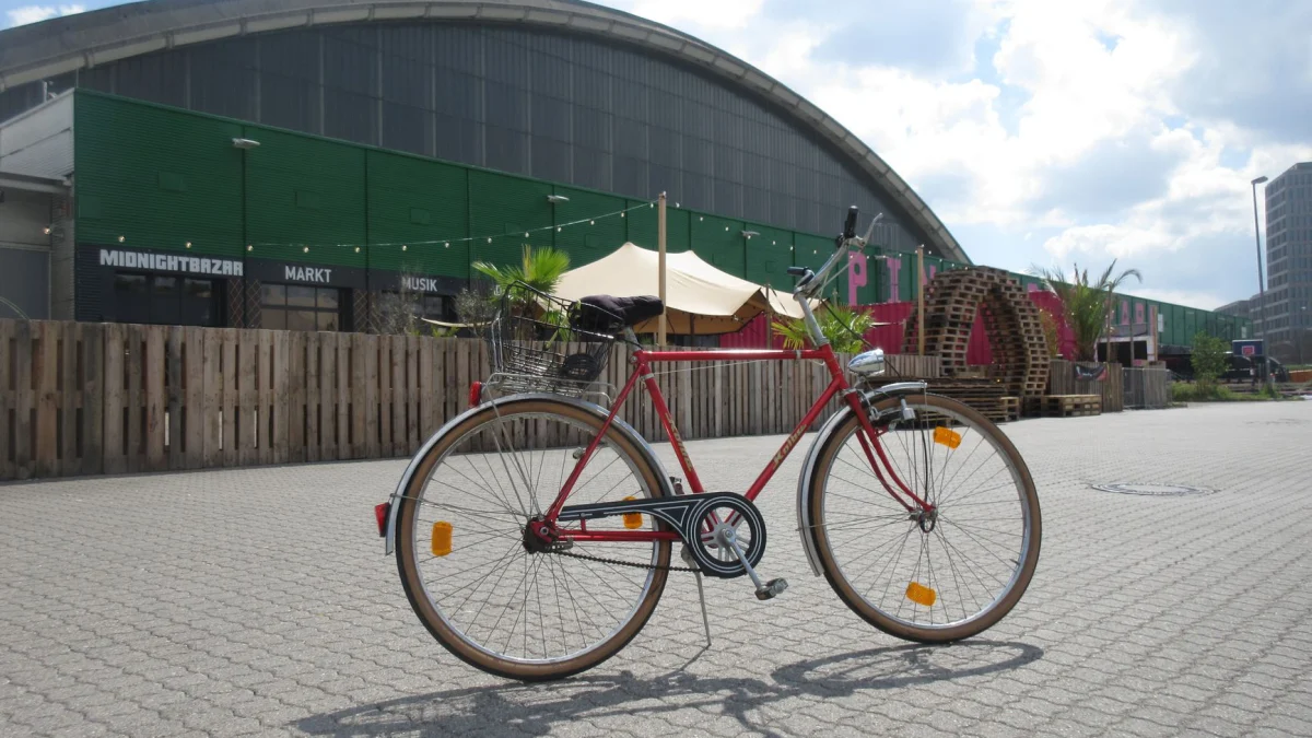 Een vintage rode fiets staat buiten geparkeerd voor een industrieel gebouw onder een blauwe hemel.