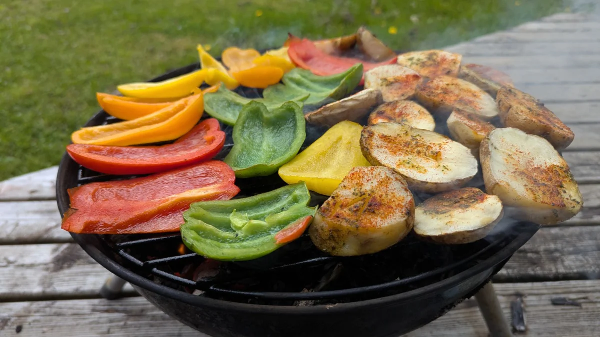 Levendige paprika's en gekruide aardappelen sissen op een barbecue buiten.
