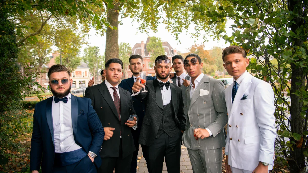 Een groep stijlvolle getuigen in kostuums poseert buiten tijdens een huwelijksceremonie en straalt elegantie uit.