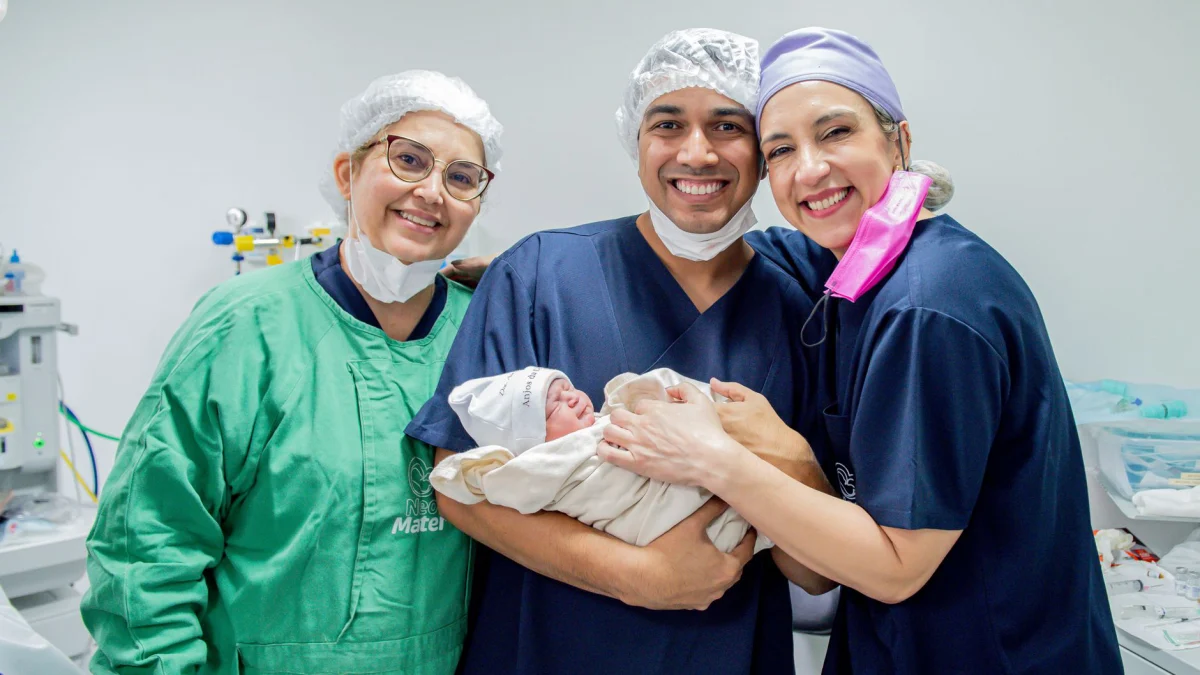 Lachende zorgprofessionals houden een pasgeboren baby vast in een ziekenhuiskamer.