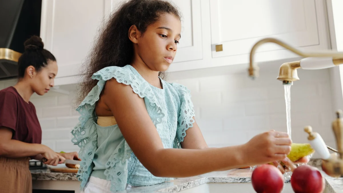 Afrikaans-Amerikaans meisje wast fruit bij de gootsteen in een elegante keuken naast een volwassene.