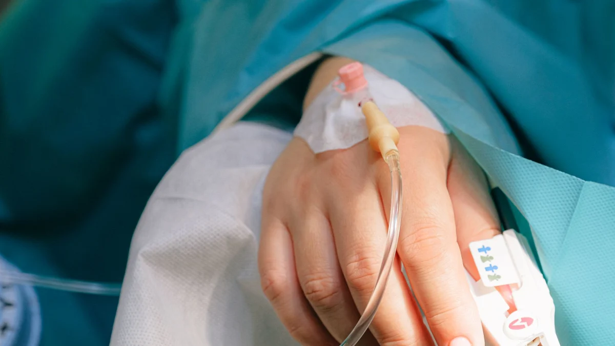 Close-up van de hand van een patiënt met intraveneuze therapie en een pulsoximeter, wat staat voor gezondheidszorg en behandeling.