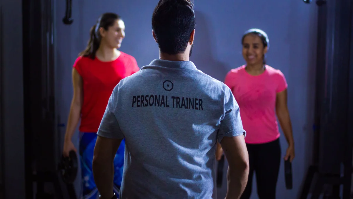 Achteraanzicht van een personal trainer die twee vrouwen begeleidt tijdens een binnensessie in de sportschool.