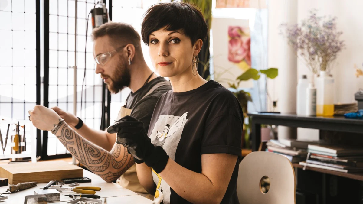 Een bebaarde man en vrouw werken samen in een zonnige studio, gebruikmakend van gereedschap.