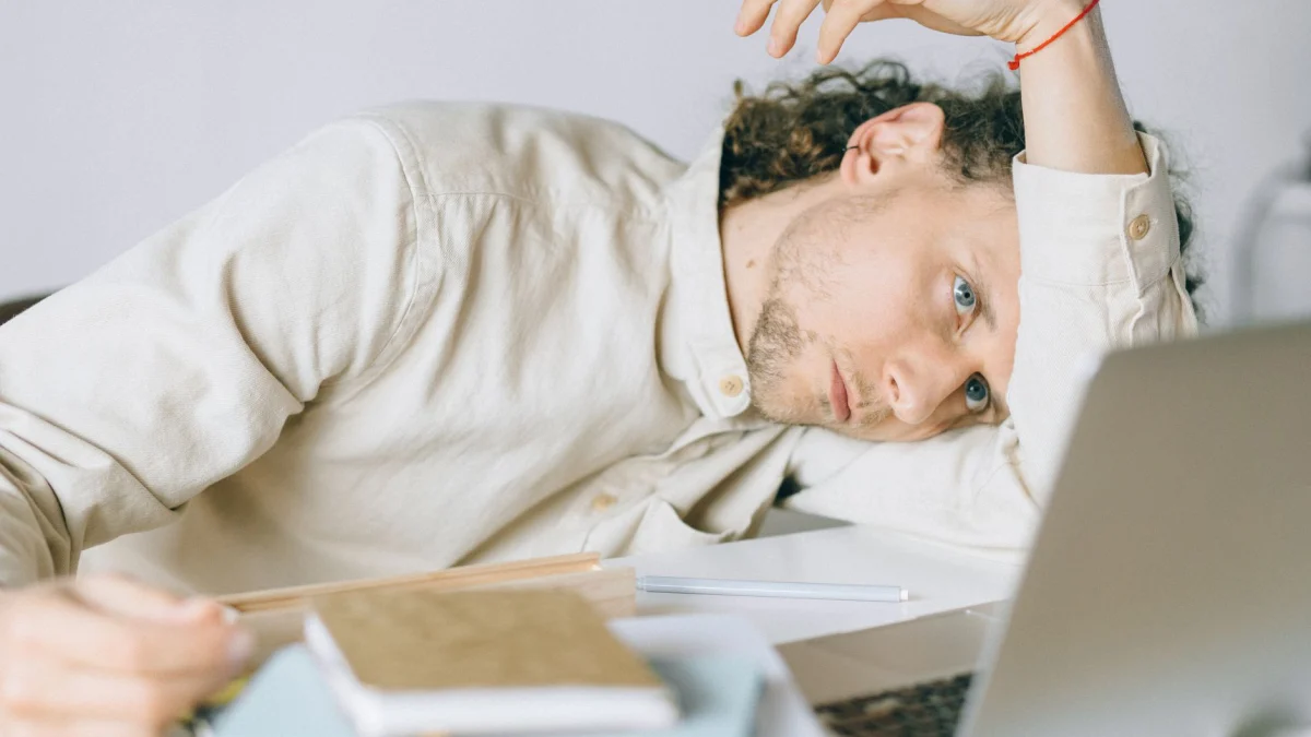 Een vermoeide Caucasische man achter een bureau, vertoont tekenen van uitputting en stress, wat een voorbeeld is van burn-out op de werkplek.