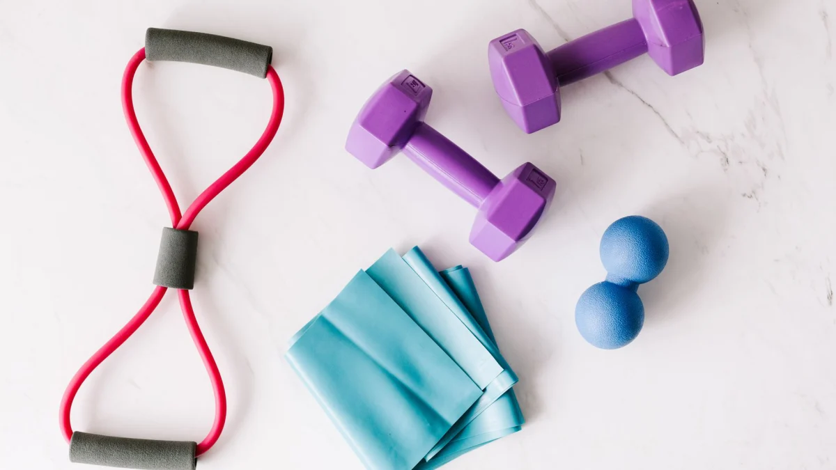 Kleurige thuis workout apparatuur, inclusief dumbbells en weerstandsbanden, op een marmeren oppervlak.