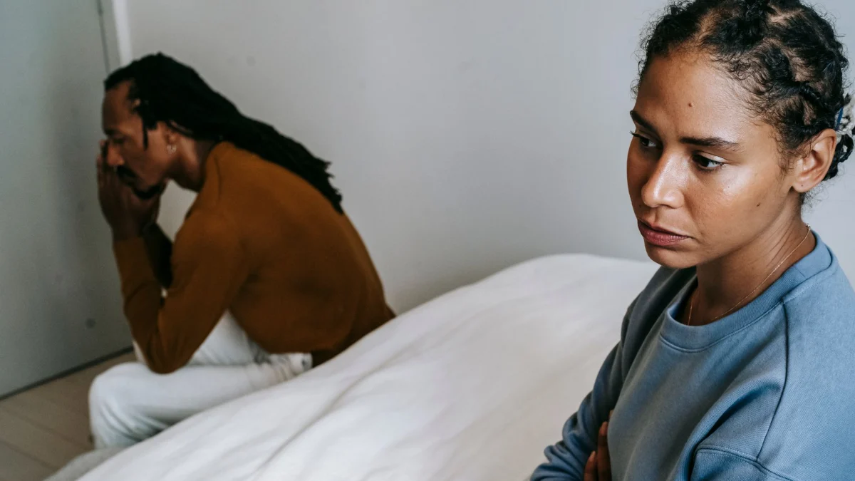 Een stel zit op bed, met een peinzende en serieuze blik, wat suggereert dat er spanning in de relatie is.