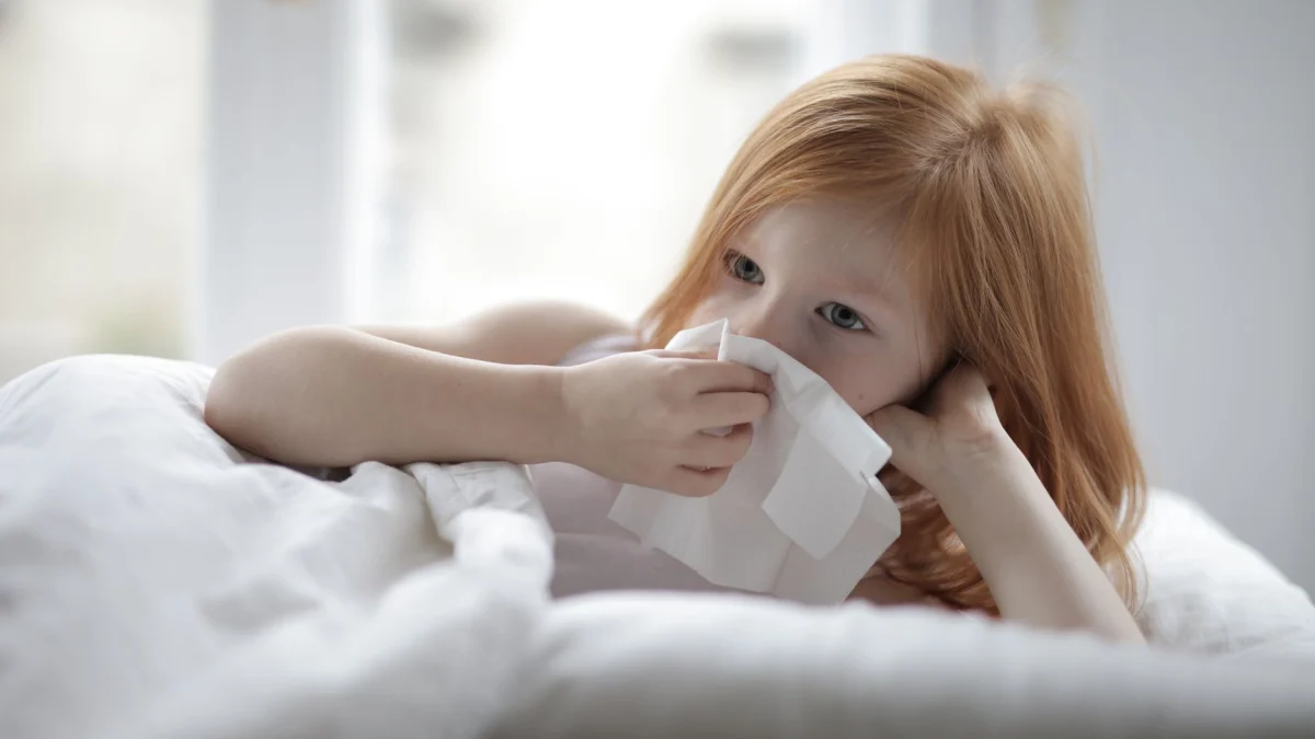 Een jong meisje met rood haar ligt in bed en gebruikt een tissue, wat suggereert dat ze zich misschien niet goed voelt.