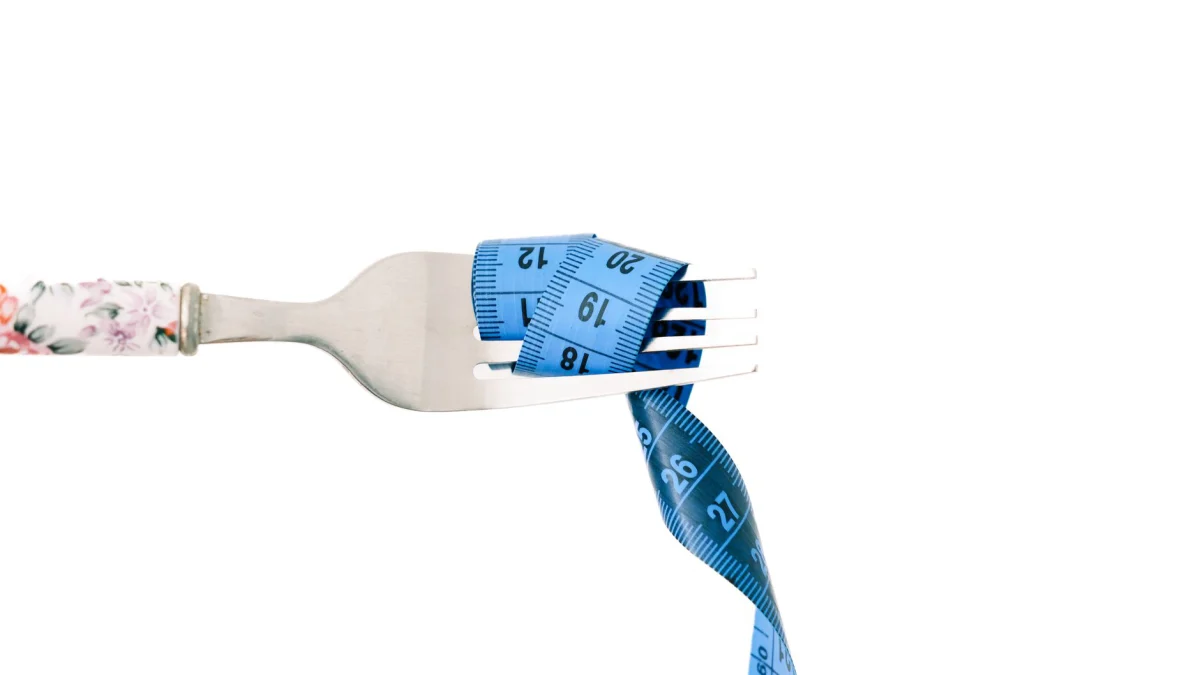 Een close-up van een vork omwikkeld met een blauw meetlint, symbool voor dieet en gewichtsbeheersing.